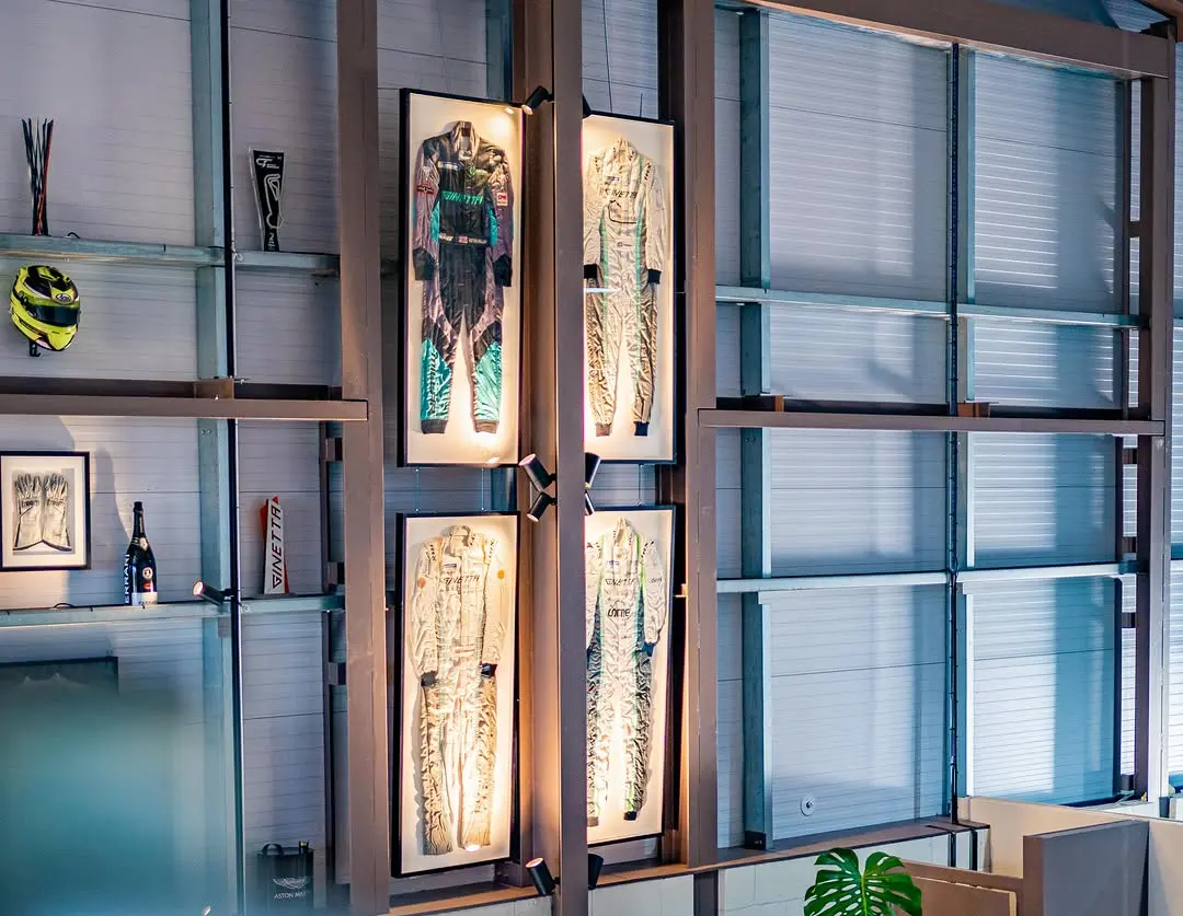 Ginetta race suits displayed in backlit cases high on the clubhouse wall, beside a helmet and a framed print of racing gloves
