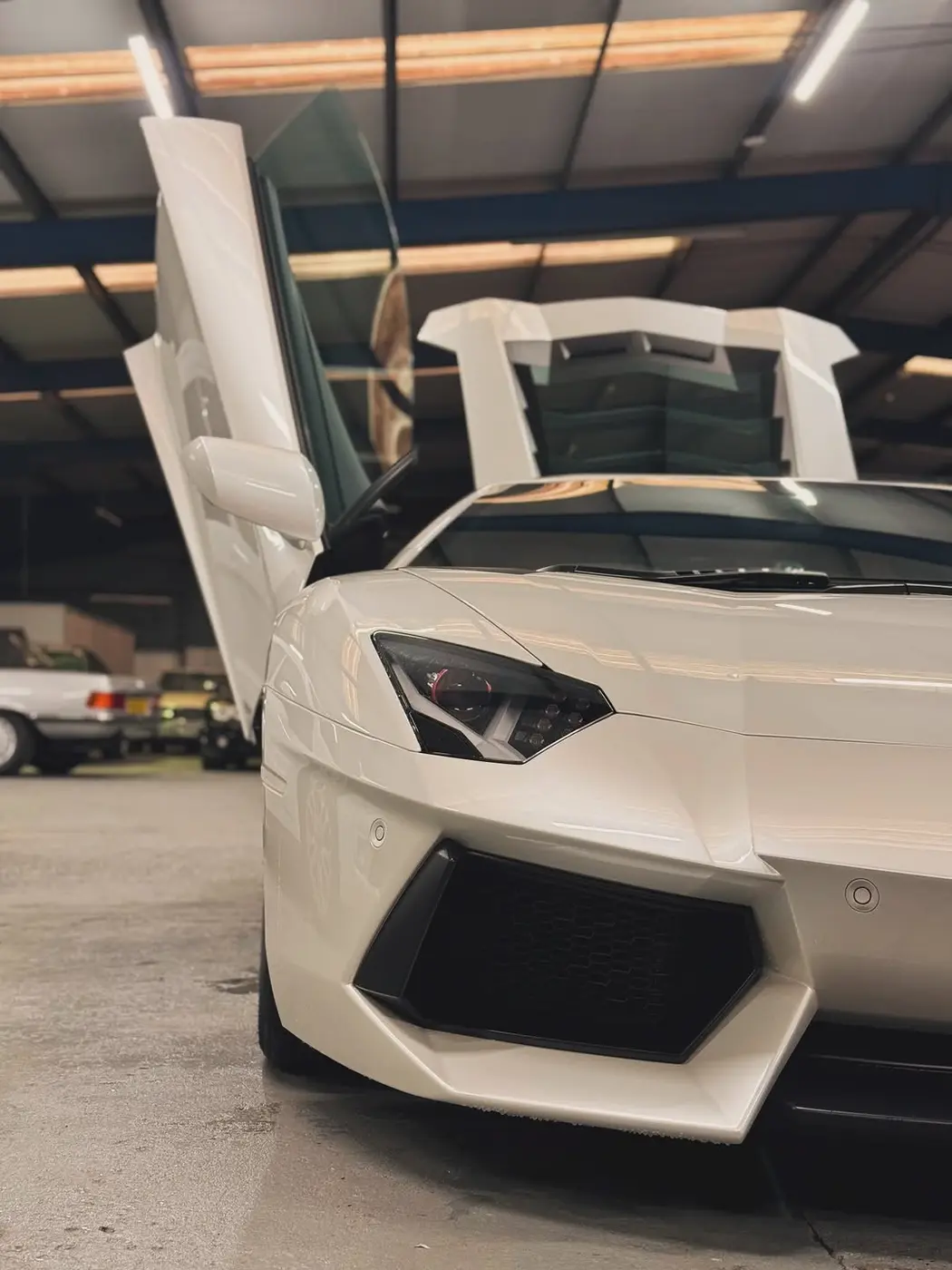 A white Lamborghini Aventador with both doors raised inside the clubhouse