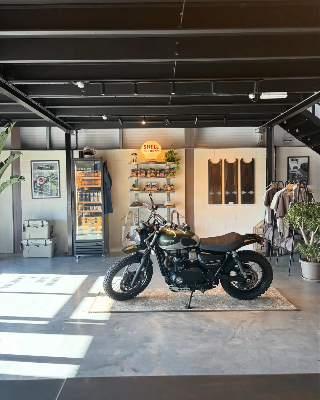 A Triumph Scrambler parked inside 45 Fuel beside the retail shelves, YETI coolers and a Shell Economy sign